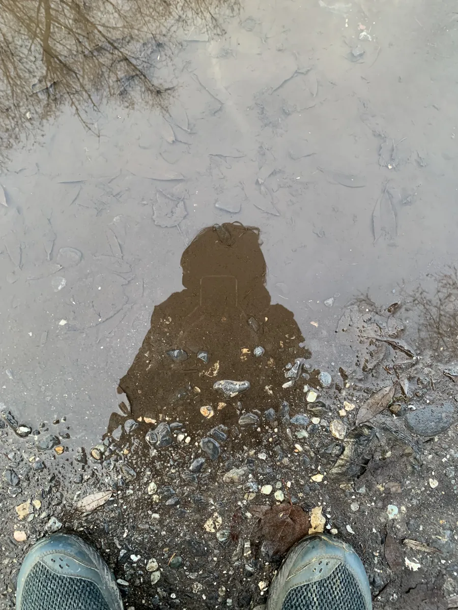 Ombre d’une personne dans une flaque, au milieu des cailloux