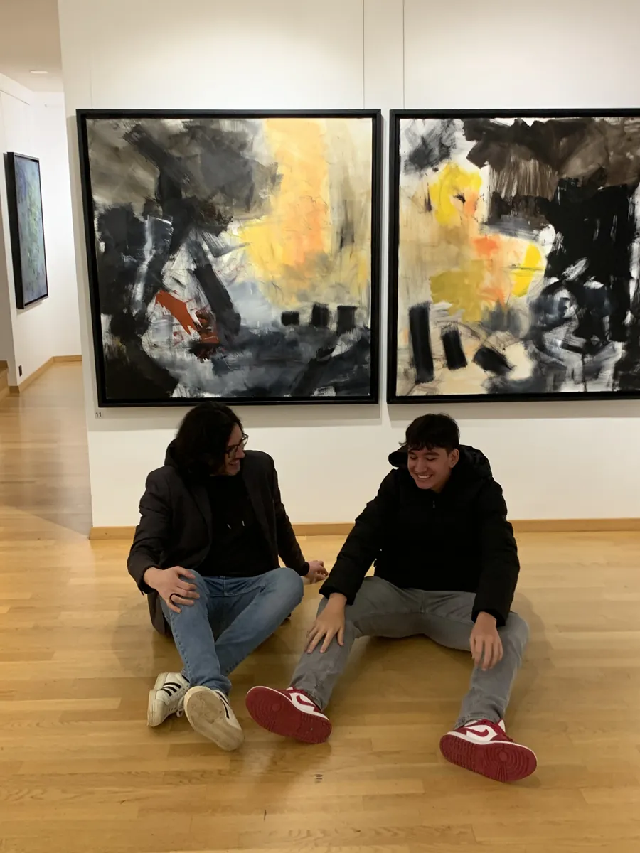 Deux personnes assises au sol devant des tableaux dans une salle d’exposition